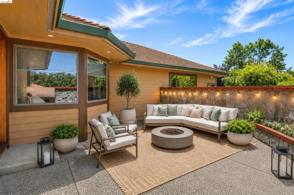 Outdoor patio featuring an exposed aggregate concrete surface, a stucco exterior, and a stone wall with a brick cap