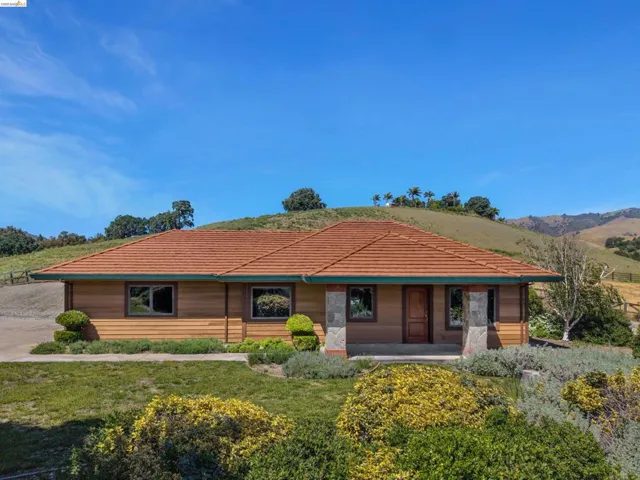 Single-story residence featuring a terracotta-hued tile roof, horizontal wood siding, and stone-clad pillars at the entry