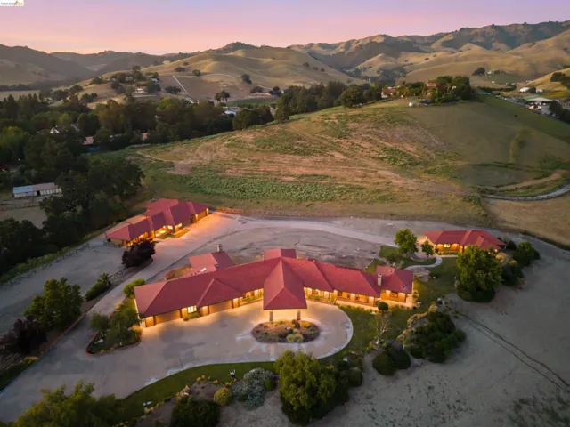 Expansive property featuring a prominent main residence with a red tile roof, circular driveway, and meticulously landscaped central island