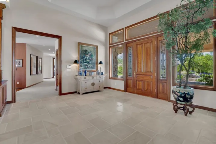 Gracious entry foyer featuring light-toned tile flooring, rich wood-framed double entry doors with decorative glass panels, and expansive windows offering outdoor views