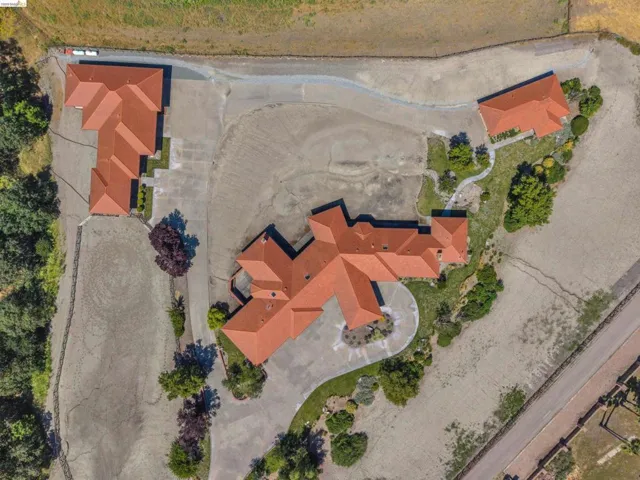Expansive property featuring three buildings with terracotta-style tile roofs, a circular driveway, multiple paved parking areas, a separate gravel driveway, and mature landscaping