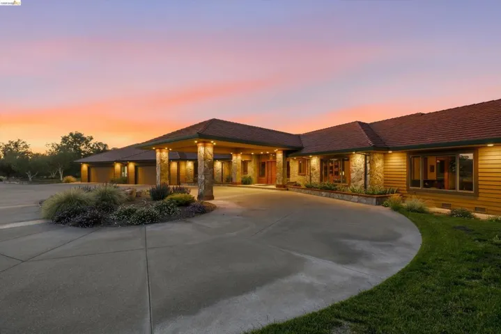 Ranch-style residence featuring a prominent covered entry with stone-clad columns, a circular concrete driveway, and exterior lighting