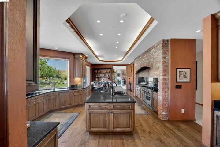 Gourmet kitchen featuring a large central island with integrated sink, stainless steel appliances, brick archway, extensive wood cabinetry, and wood-finish flooring