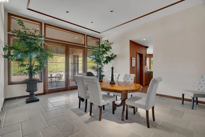 Spacious room featuring light-toned tile flooring, extensive wood-framed windows, and French doors leading to an outdoor patio