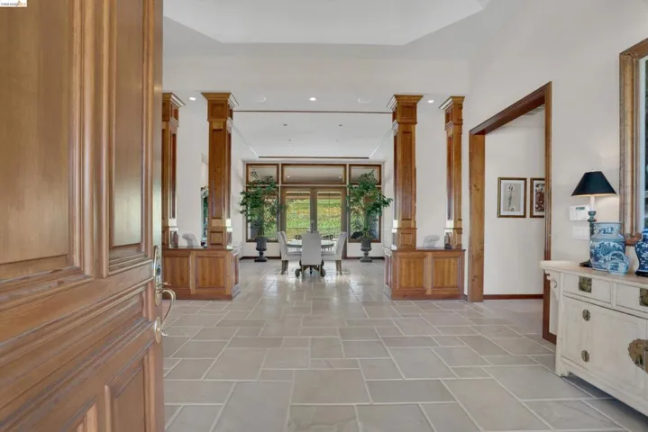 Grand entryway featuring light-toned tile flooring set in a pattern, a paneled wood-finish door, and architectural wood-finish columns with integrated cabinetry