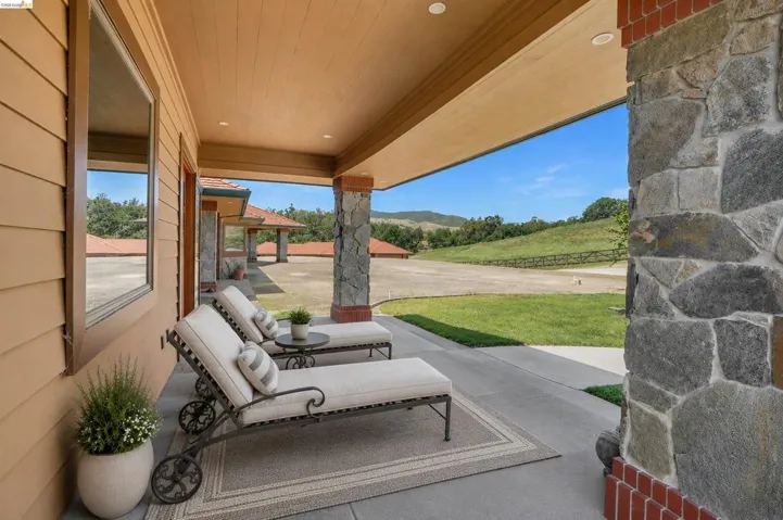 Expansive covered patio featuring stone columns with brick accents, recessed lighting, and a concrete floor