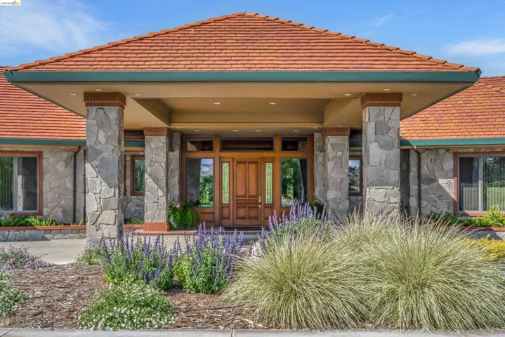 Stone-clad exterior featuring a prominent covered entry with four stone pillars and brick accents