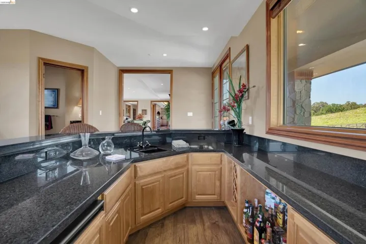 Wet bar featuring dark granite countertops, an undermount sink, recessed lighting, wood-finish flooring, and natural wood cabinetry