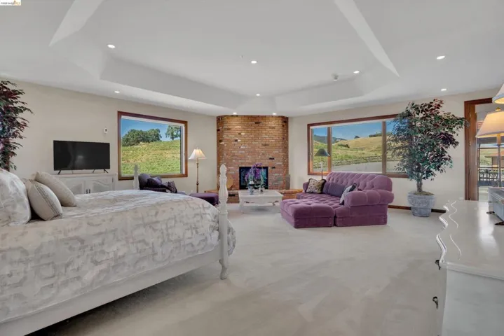 Expansive room featuring a tray ceiling with recessed lighting, a corner brick fireplace, and multiple picture windows