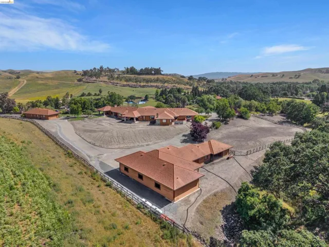 Expansive property featuring multiple structures with terra cotta tile roofing, surrounded by rolling hills and mature trees