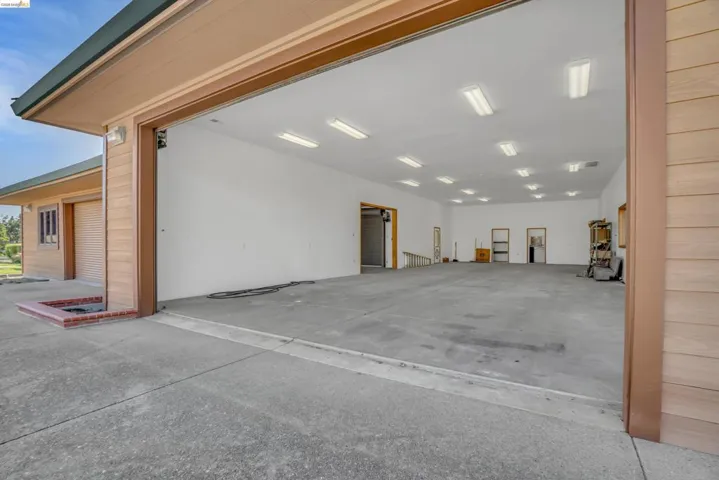 Spacious garage featuring a high ceiling, ample fluorescent lighting, concrete flooring, and multiple entry points