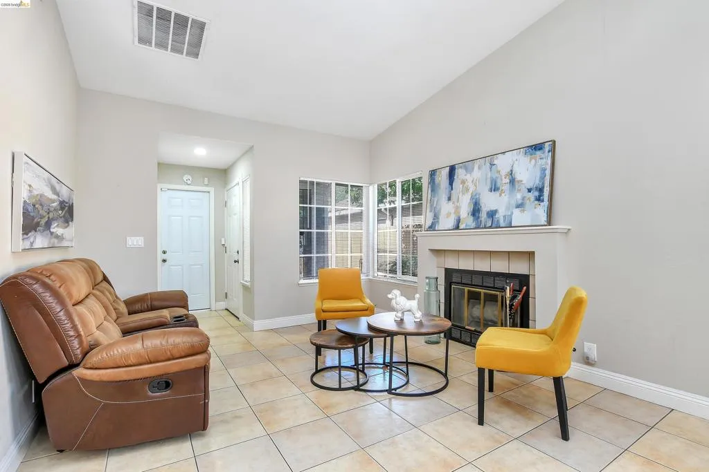 Living area featuring vaulted ceilings, tile flooring, a fireplace with a tile surround and mantle, and large windows providing natural light