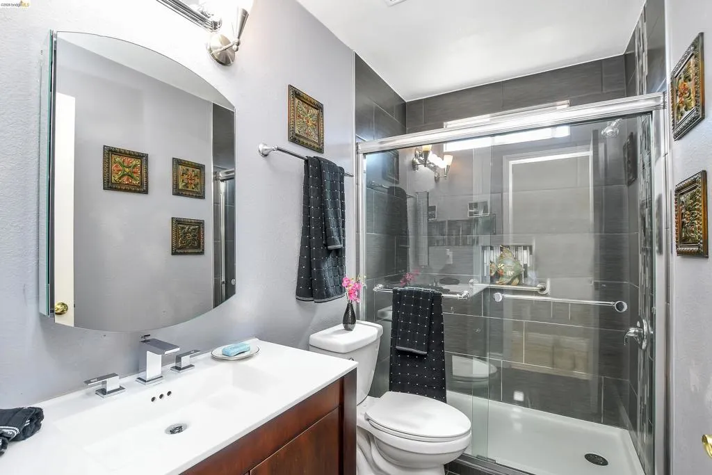 Full bathroom featuring a walk-in shower with dark tile surround and glass enclosure, a vanity with a white countertop and integrated sink, and a wall-mounted mirror