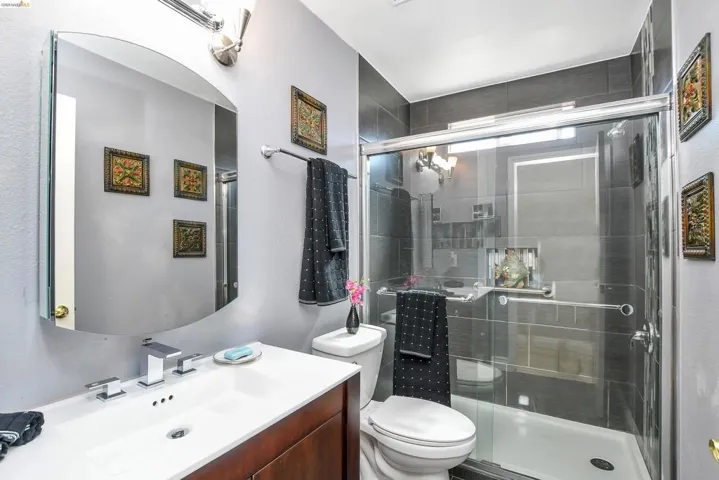 Full bathroom featuring a walk-in shower with dark tile surround and glass enclosure, a vanity with a white countertop and integrated sink, and a wall-mounted mirror