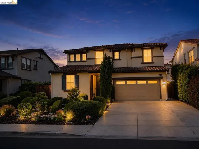 Two-story stucco residence featuring a tile roof, an attached two-car garage, manicured landscaping, and a concrete driveway