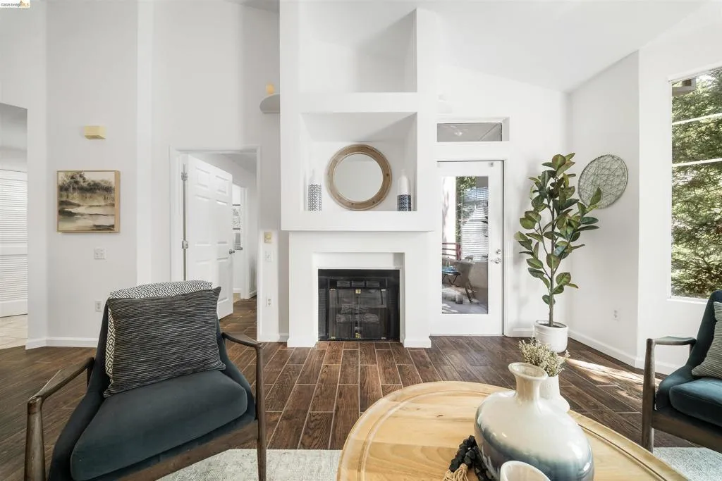 Living room featuring wood finish floors, vaulted ceiling, and a glass covered fireplace