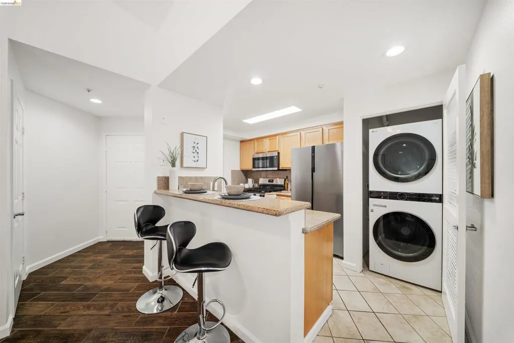 Kitchen featuring stainless steel appliances, stacked washer / drying machine, a peninsula, a kitchen bar, and recessed lighting