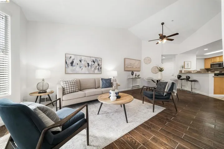 Living area featuring a ceiling fan, dark wood-style flooring, and vaulted ceiling