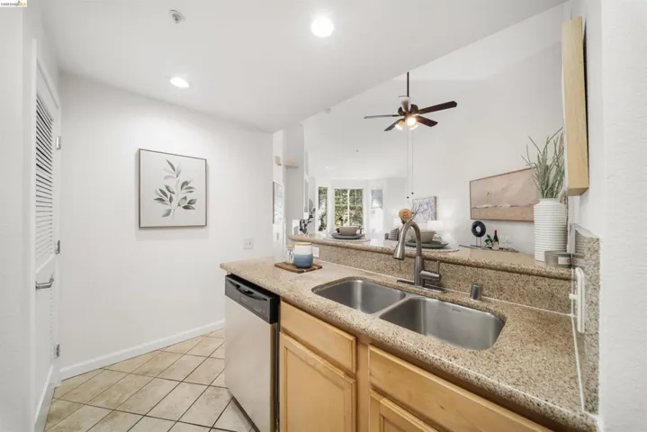 Kitchen with light wood finish cabinets, stainless steel dishwasher, light stone countertops, open floor plan, and recessed lighting