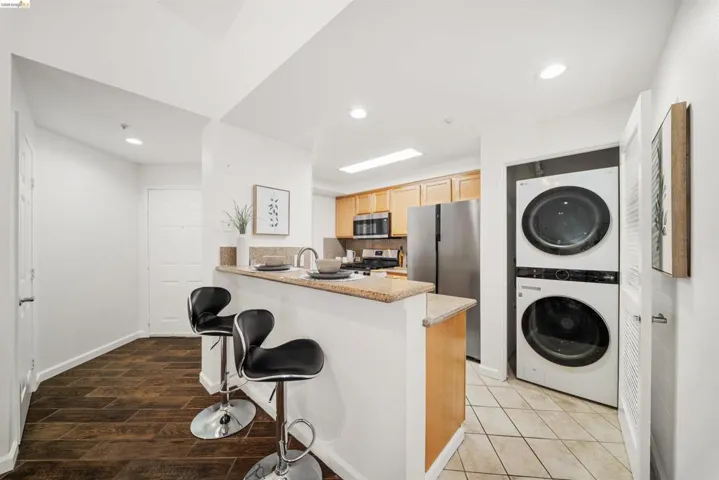 Kitchen featuring stainless steel appliances, stacked washer / drying machine, a peninsula, a kitchen bar, and recessed lighting