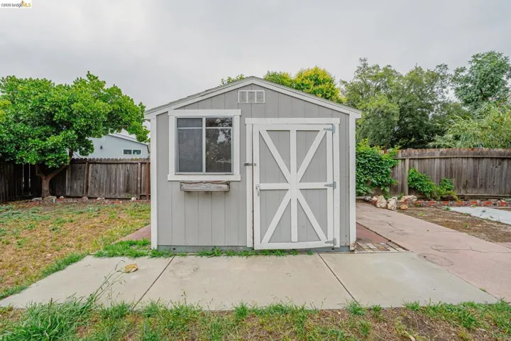 Detached utility shed with a gable roof, light gray siding, and white trim