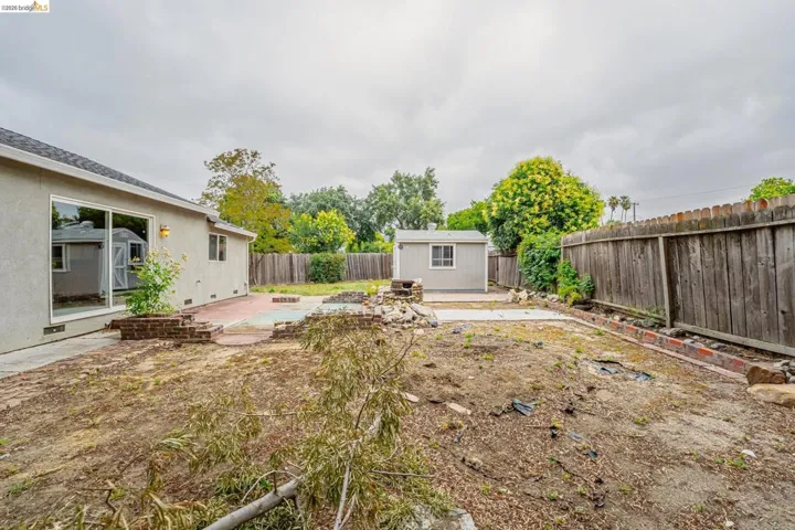 Expansive backyard featuring a stucco exterior with sliding glass doors, a detached storage shed, a brick patio, and a wood privacy fence