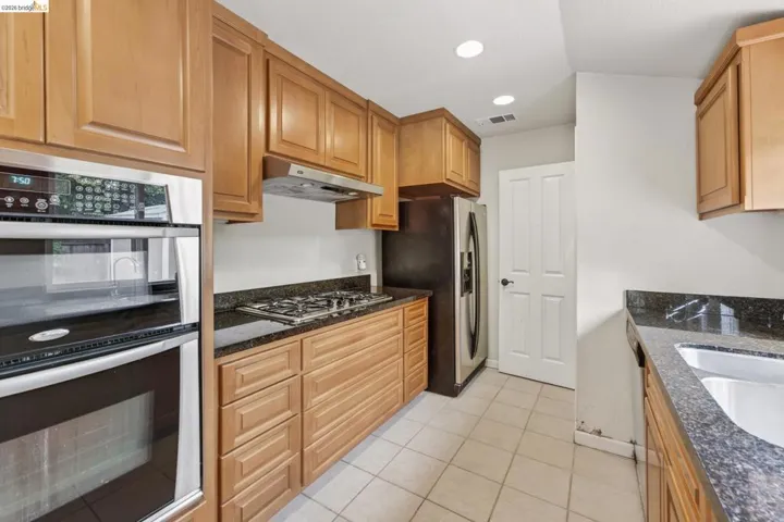 Kitchen featuring wood cabinetry, dark countertops, stainless steel appliances, and a double basin sink