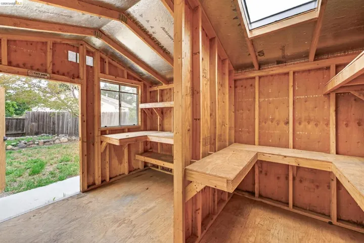 Interior shed framing featuring an open doorway, a single window, built-in shelving, and a skylight