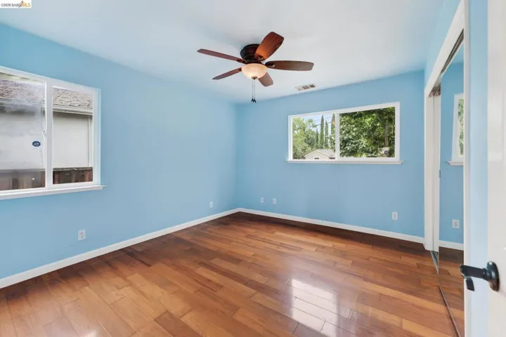 Spacious room featuring wood-finish flooring, light blue walls, and a ceiling fan with integrated lighting