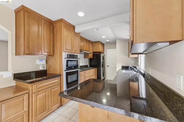 Kitchen featuring extensive light wood cabinetry, dark speckled countertops, built-in stainless steel double oven, and recessed lighting