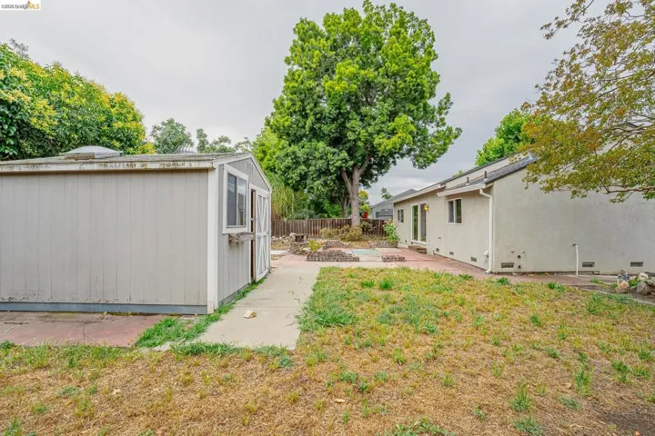 Expansive yard featuring a detached storage shed, concrete patio area, and mature trees