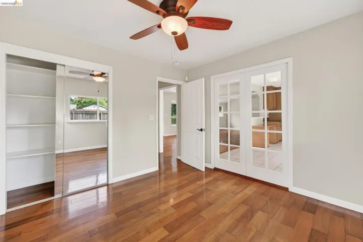 Room featuring wood-finish flooring, a ceiling fan with integrated lighting, and a mirrored sliding closet door