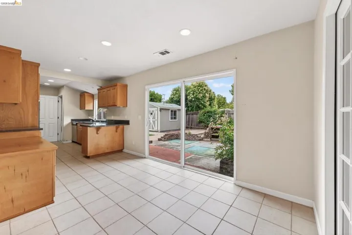 Kitchen with light wood cabinetry, dark countertops, and tile flooring, featuring a double basin sink and built-in dishwasher
