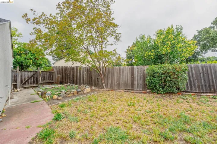 Rear yard featuring a wooden fence, mature tree, and a garden bed bordered by rocks