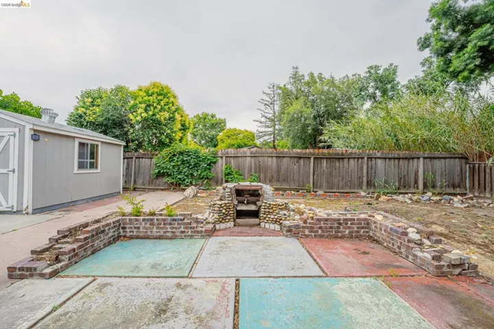 Exterior featuring a detached shed with a window and white double doors, a concrete patio with multicolored sections, and a stone and brick-built structure