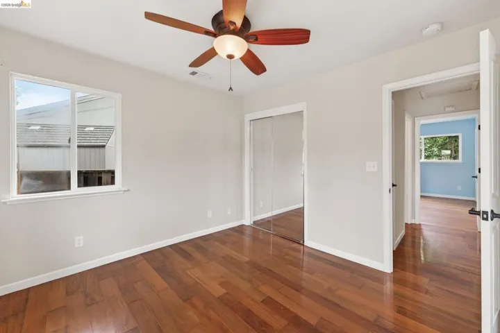 Bedroom featuring wood-finish flooring, a ceiling fan with light fixture, and a window with white trim
