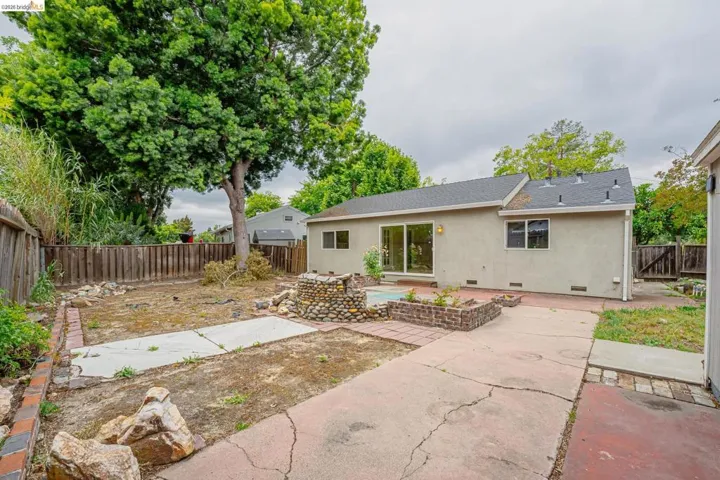 Expansive backyard featuring a stucco exterior, dark shingle roof, sliding glass patio door, and a stone-clad water feature