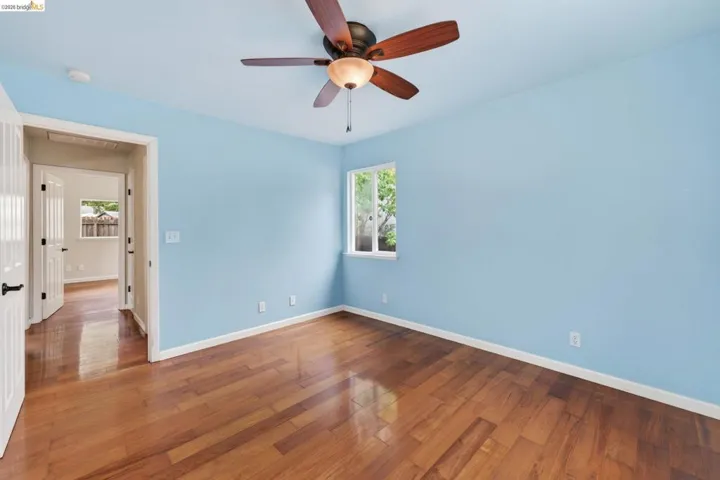 Interior room featuring wood-finish flooring, a ceiling fan with light fixture, and a window with white trim