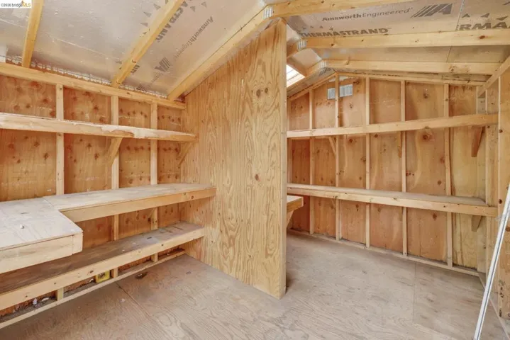 Interior storage shed featuring wood-finish walls and flooring, built-in shelving, and exposed ceiling rafters