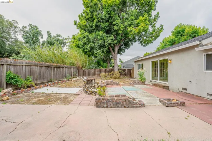Spacious backyard featuring a large concrete patio, mature tree, and privacy fencing