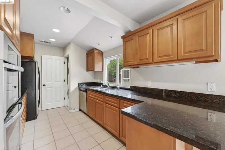 Kitchen featuring granite-style countertops, wood cabinetry, stainless steel oven, and recessed lighting