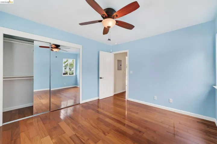 Room featuring wood-finish flooring, a ceiling fan with integrated lighting, and a window with white trim