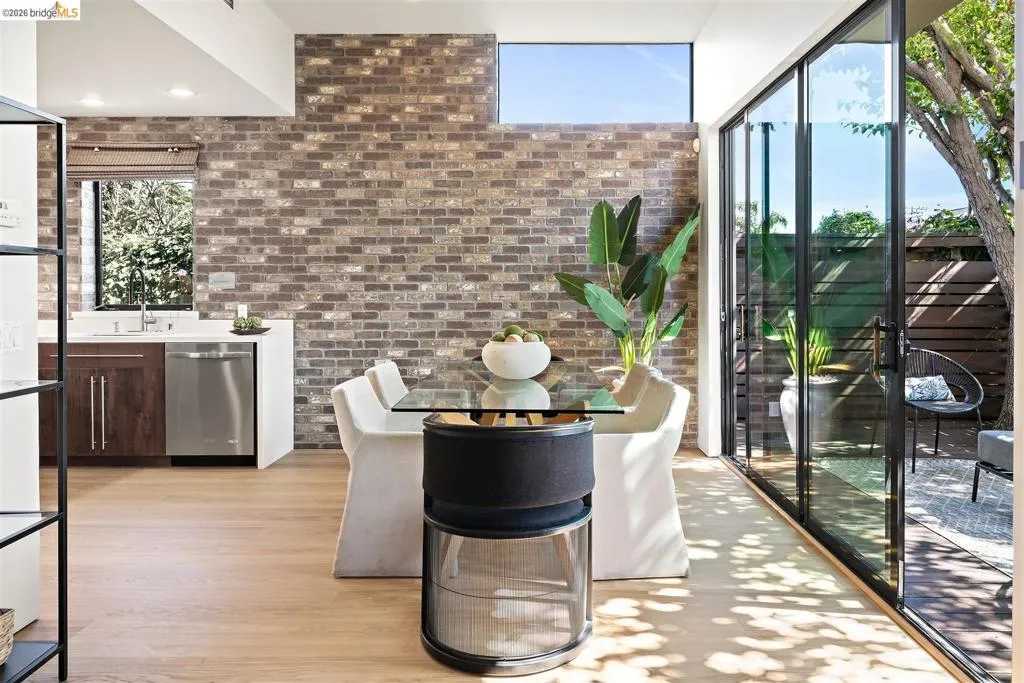 Open-concept living space featuring wood-finish flooring, an exposed brick accent wall, and a full wall of black-framed sliding glass doors