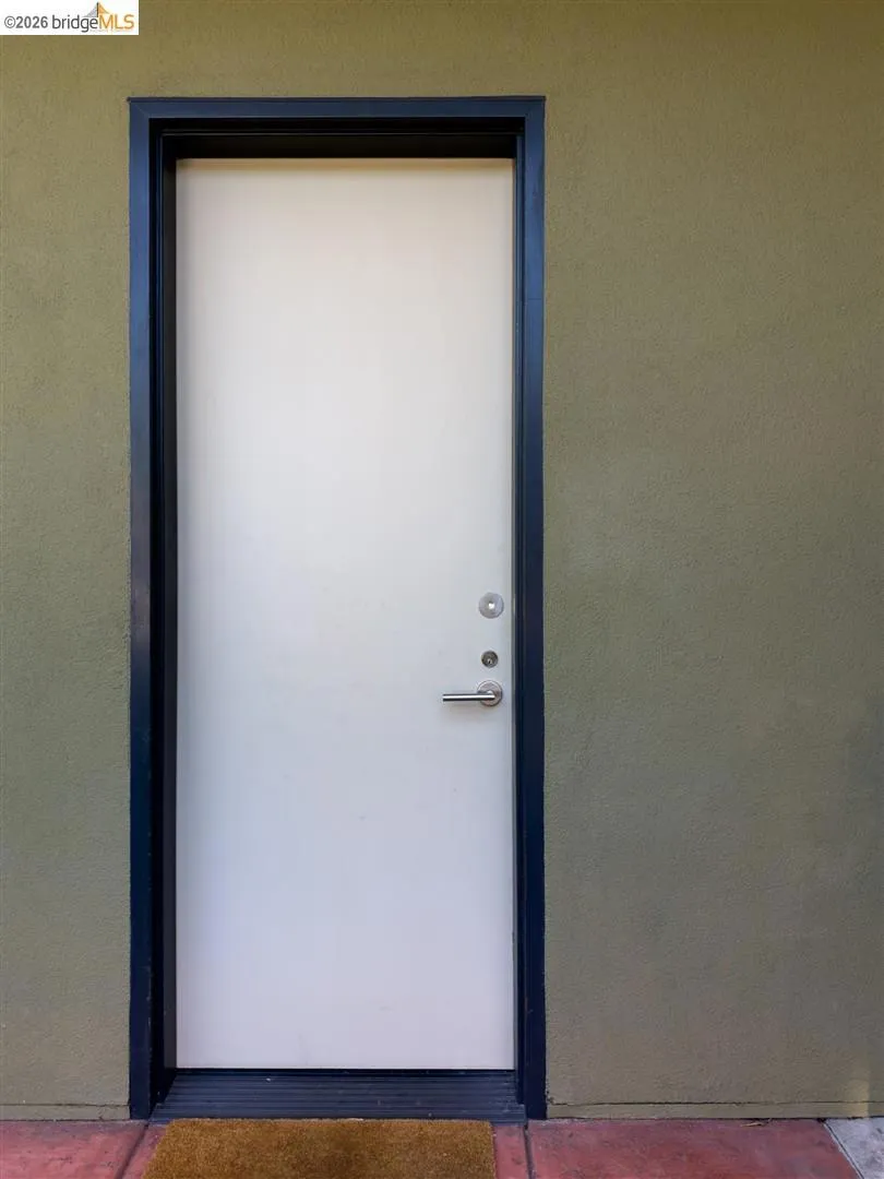 White entry door with a black frame, brushed nickel hardware, and an olive-toned stucco exterior