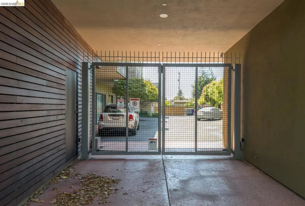 Gated entry to a covered parking area featuring a concrete floor, recessed lighting, a wood-slat accent wall, and a side access door