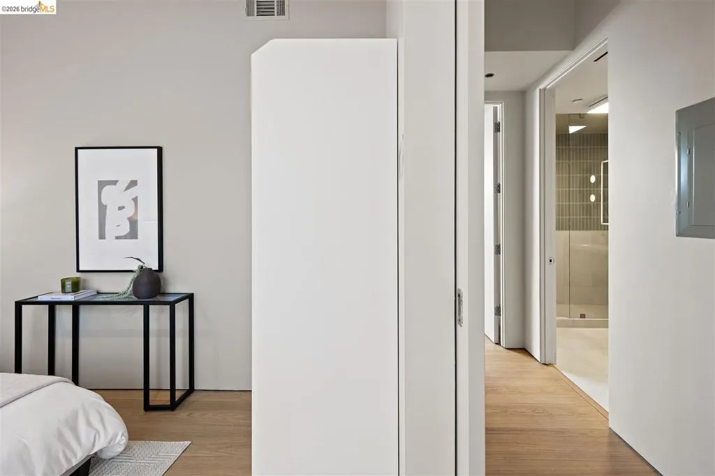 Warm wood-finish flooring extends through the hallway, featuring a modern bathroom with vertical tile accents, a glass shower enclosure, and recessed lighting