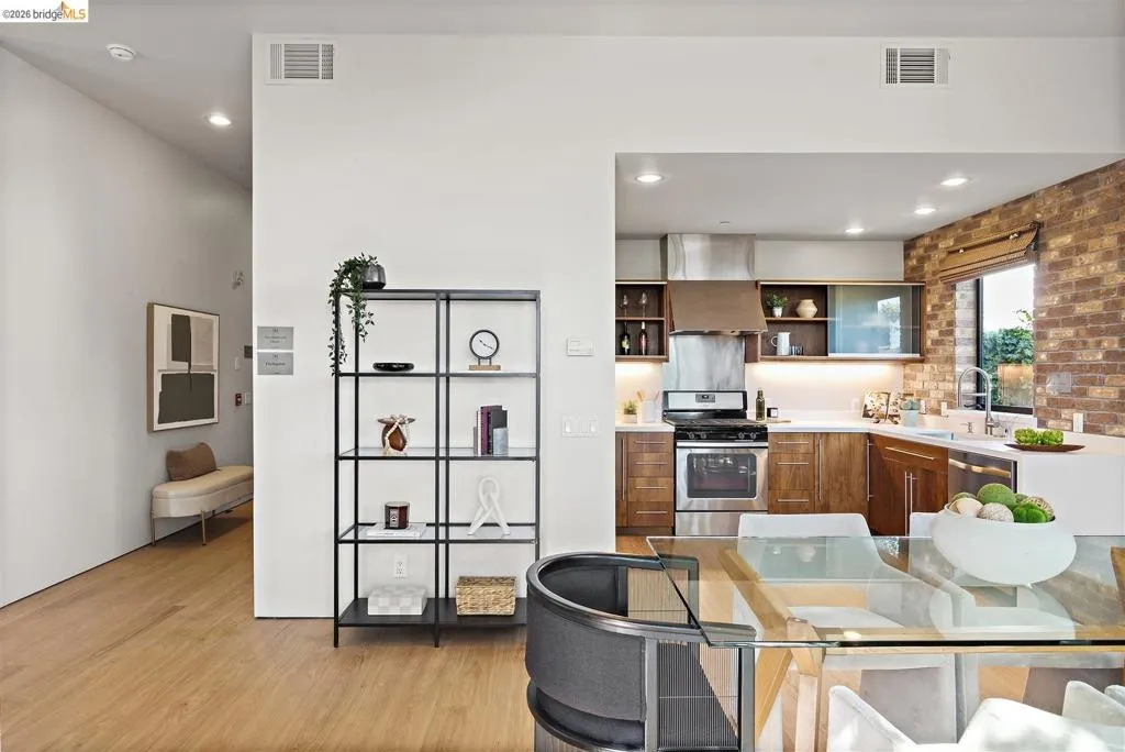 Open-concept kitchen featuring stainless steel appliances, wood cabinetry, stone countertops, and a brick accent wall