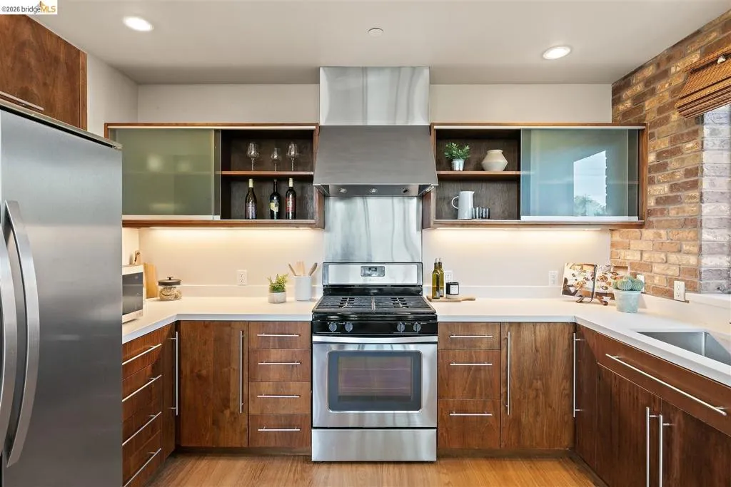 U-shaped kitchen featuring stainless steel appliances, wood-finish cabinetry, light countertops, and a brick accent wall