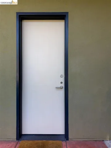 White entry door with a black frame, brushed nickel hardware, and an olive-toned stucco exterior