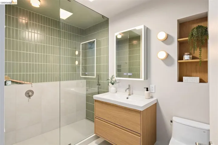 Contemporary bathroom featuring a glass-enclosed shower with vertical subway tile, a wood-finish vanity with an integrated sink, an illuminated medicine cabinet, and recessed wood shelving